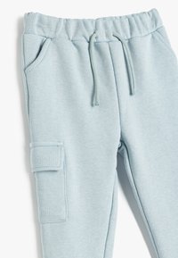 Helle blaue Sweatpants aus weichem Stoff, mit einem elastischen Bund, Kordelzug, seitlichen Taschen und einer Cargo-Tasche am Oberschenkel.