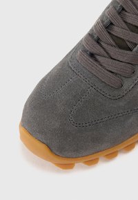 Baskets en daim gris avec un bout arrondi, une tige texturée et une semelle en caoutchouc brun dotée de petites protubérances pour la traction. Les lacets sont gris foncé.