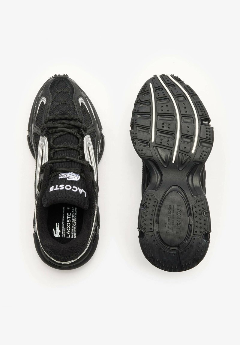 Chaussures de sport noires avec une tige en mesh, des accents argentés et une semelle en caoutchouc noire texturée. Les caractéristiques incluent une languette rembourrée et un logo.