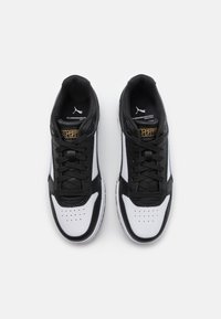 Black and white sneakers with a smooth leather upper, mesh panels, perforated toe, flat laces, and gold accents on the tongue.