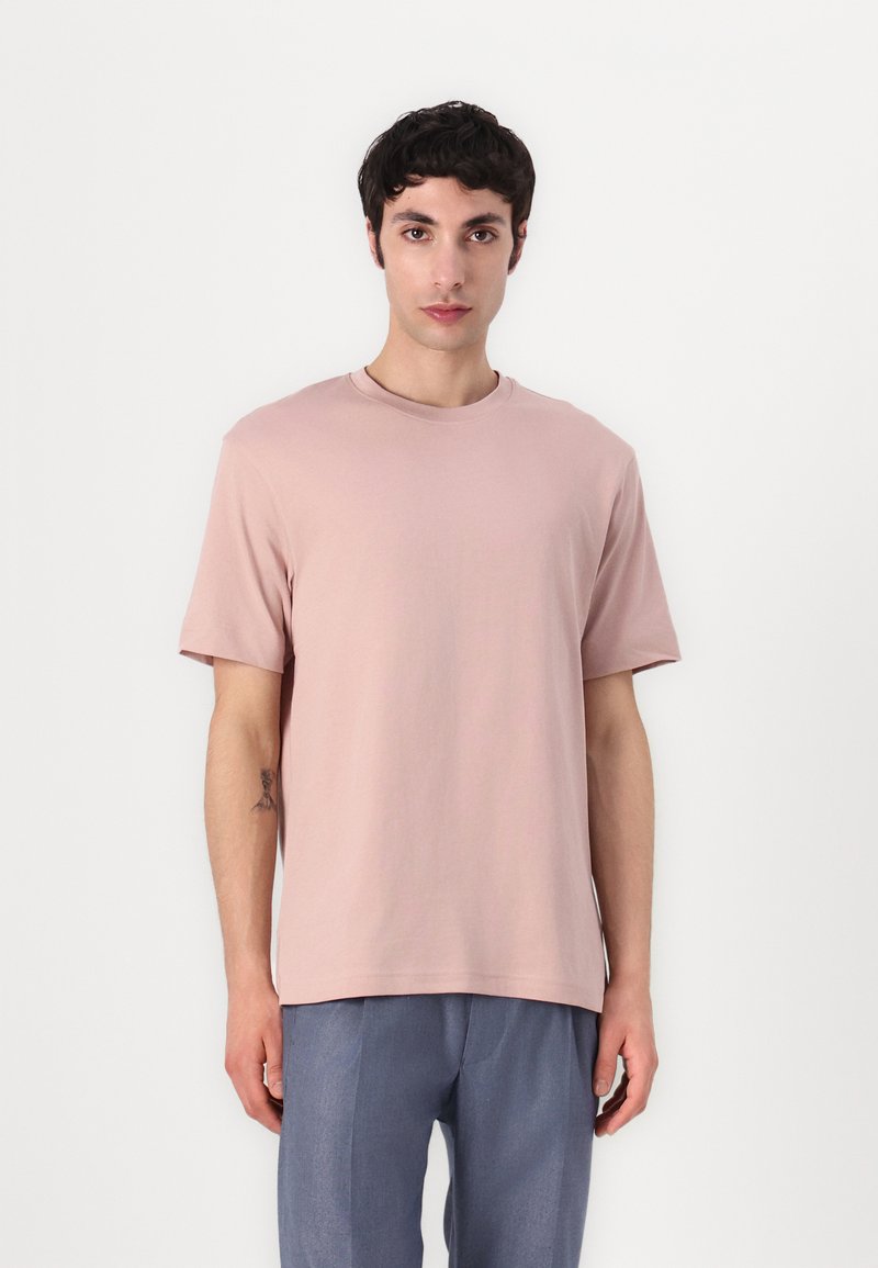 Rosa Baumwoll-T-Shirt mit kurzen Ärmeln, rundem Hals, glatter Textur und lockerer Passform, kombiniert mit hellblauen Hosen.