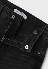 Schwarze Denim-Jeans mit Reißverschluss, Knopfverschluss und metallischen Beschlägen. Textil mit strukturiertem Material, glatter Oberfläche und minimalistischem Design.