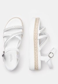 Sandali bianchi con cinturini incrociati, borchie metalliche e una suola in juta avvolta, dotati di chiusura con fibbia sul cinturino alla caviglia.