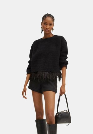 Maglione nero a maglia con finitura testurizzata e rifiniture in piume. Abbinato a pantaloni corti neri e stivali neri al ginocchio, mentre tiene una borsa nera.