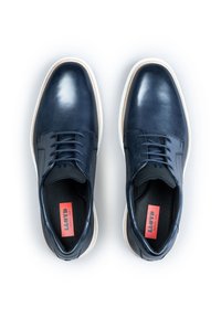 Chaussures en cuir bleu marine avec une finition lisse, à lacets, semelle blanche contrastante et branding rouge visible à l'intérieur.