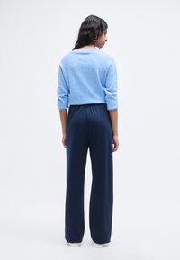 Ανοιχτό μπλε πουλόβερ με μανίκια τριών τετάρτων, σε συνδυασμό με σκούρο μπλε παντελόνι φαρδύ στο πόδι. Απαλό, υφασμάτινο με υφή και χαλαρή εφαρμογή, με ελαστική μέση.