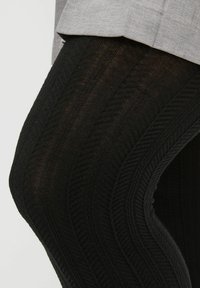 Czarne legginsy z fakturą w zygzak, z prążkowanym wzorem. Częściowo zakryte szarym topem, podkreślającym fakturę i dopasowanie.