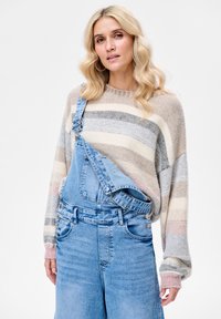 Sweter dziany w paski w kolorach beżu, jasnoróżowym, niebieskim i szarym; połączony z niebieskimi ogrodniczkami z denimu z regulowanymi szelkami i bocznymi guzikami.