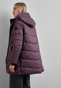 Puffjacka i mörklila med huva, utrustad med quiltat mönster, dragkedja framtill och sidofickor. Slät textur med en svart accentlogotyp.