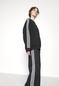 Felpa nera e pantaloni della tuta coordinati, entrambi con righe bianche lungo i lati. Vestibilità comoda, tessuto morbido, design a gamba larga.