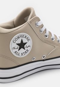 Béžové kožené vysoké tenisky s bílými tkaničkami, texturovaným límcem, nášivkou černé hvězdy, stříbrnými očky a černobílou pruhovanou podešví.