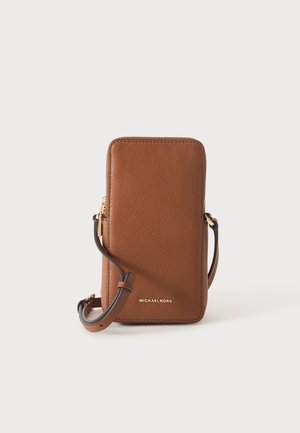 Sac bandoulière pour téléphone Michael Kors en cuir marron avec fermeture éclair dorée et sangle réglable sur un fond uni clair.