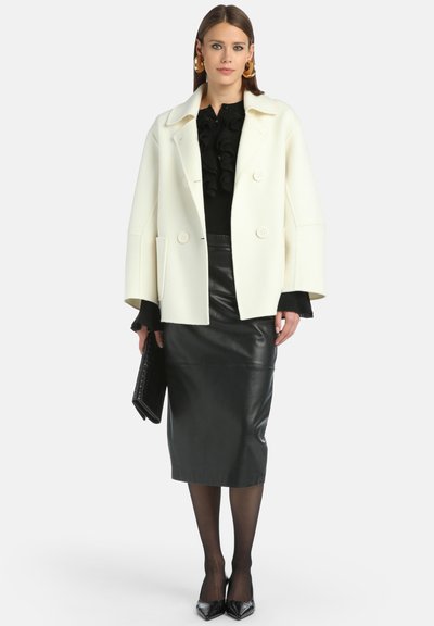 Valkoinen kaksoisnappinen takki, musta röyhelötoppi, musta nahkainen kynähame, mustat sukkahousut ja mustat kärki-korkokengät. Pitää mustaa clutch-laukkua.