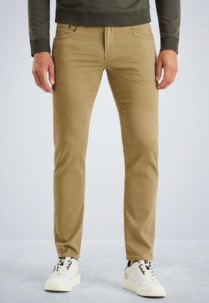 Pantaloni di cotone color beige con una vestibilità slim, dotati di cinque tasche, chiusura con zip e cuciture a contrasto, abbinati a sneakers bianche.