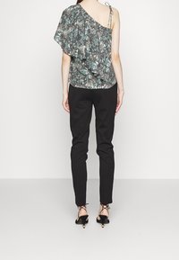 Blommönstrad, enaxlad topp i grön och svart, med en rynkad design och en fastsydd volang. Kombinerad med svarta slim-fit byxor och klackar.