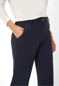 Pantalon bleu marine avec une texture lisse, comportant une poche avant, des passants de ceinture et une fermeture à bouton à la taille.