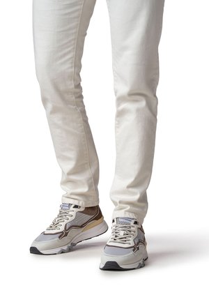 Sneakers grigie e marroni con dettagli in mesh e pelle, caratterizzate da un design con lacci e suola strutturata, abbinate a jeans bianchi a taglio slim.