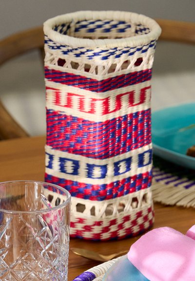Woven cylindrical basket with white, red, and blue patterns. Features openwork accents and textured surface. Sturdy base.