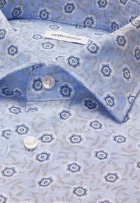 Chemise bleu clair avec un motif floral bleu foncé et gris, boutons blancs, et une étiquette "seidensticker" à l'intérieur du col.
