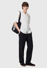 Witte blouse met korte mouwen en een knoopsluiting, gecombineerd met zwarte spijkerbroeken met een losse pasvorm en zwarte sneakers. Model draagt een zwarte tote-tas.