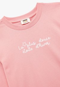 Lyserød sweatshirt med rund halsudskæring, prydet med hvid tekst "La plus douce étoile d'hiver" og en stjerneaccent. Blødt bomuldsstof.
