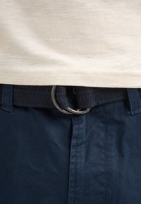 Navy blue pants with a textured waistband and silver metal ring buckle, paired with a light beige shirt just above the waist.