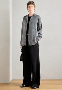 Camicia a righe bianco e nera con bottoni, abbinata a pantaloni neri larghi. Una piccola borsa nera e scarpe a punta con dettagli in argento completano il look.