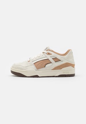 Witte en beige sneaker met suede en mesh materialen, een chunky zool, en uitsparingen aan de zijkant met een gebrandmerkte hiel en veters.