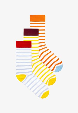 Trzy kolorowe skarpetki w paski ułożone jedna na drugiej, z czerwonymi, żółtymi i pomarańczowymi mankietami oraz dopasowanymi akcentami na palcach, na białym tle.