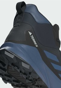 Zapato de senderismo negro y azul con una parte superior sintética texturizada, una suela de goma resistente y un prominente logo "TERREX" en el lateral.