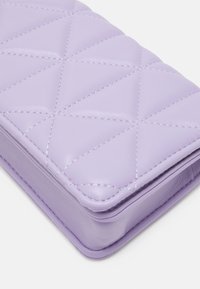 Portefeuille en cuir matelassé lavande avec motif en losange, présentant une texture lisse et des coutures le long des bords.