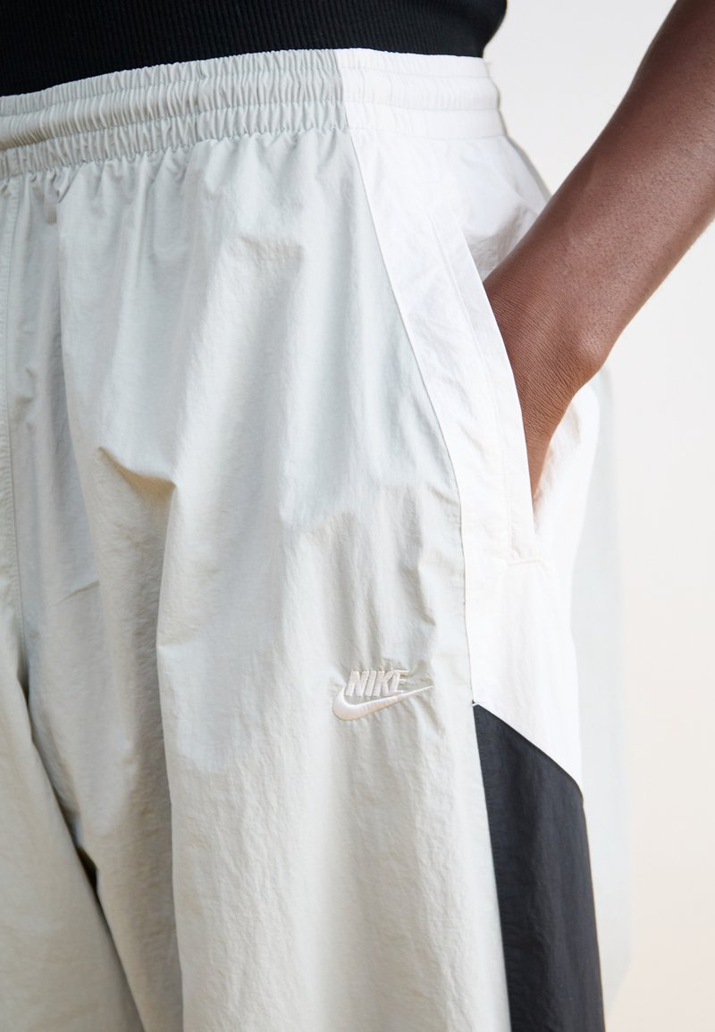 Pantalons de jogging Nike gris clair avec taille élastique, poches latérales et un détail de panneau noir. Présente le logo brodé dans une couleur claire.