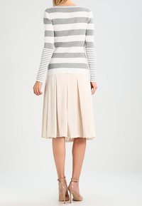 Maglione a righe grigie e bianche con coste abbinato a una gonna beige plissettata, lunga fino al ginocchio. Sandali con tacco trasparente completano il look.