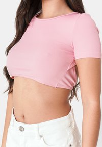 Top corto a coste rosa con maniche corte, dotato di scollatura rotonda e ritagli laterali. Abbinato a pantaloni di jeans bianchi a vita alta.
