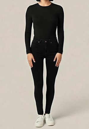 Body noir à manches longues associé à un jean noir taille haute, avec une coupe ajustée et porté avec des baskets blanches.