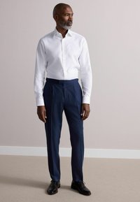 Weißes Hemd mit Knöpfen, kombiniert mit marineblauen Faltenhosen und schwarzen Schuhen. Das Outfit zeichnet sich durch eine maßgeschneiderte Passform und einen glatten Stoff aus.