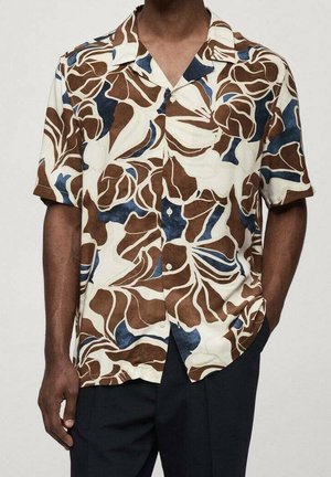 Chemise boutonnée à manches courtes à motif floral abstrait marron, bleu marine et crème portée avec un pantalon noir, mains détendues le long du corps.