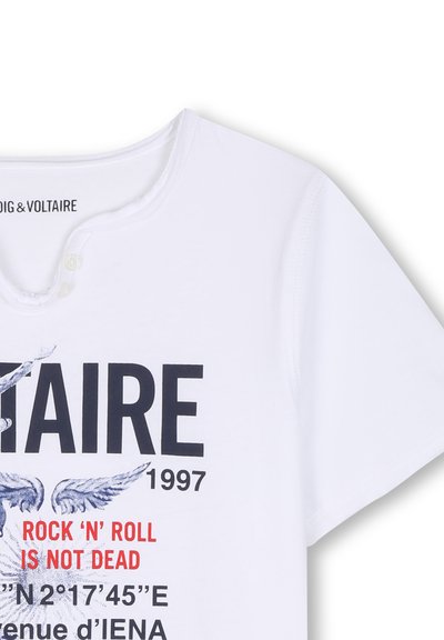 Λευκό κοντομάνικο μπλουζάκι με κείμενο "ROCK 'N' ROLL IS NOT DEAD", μαύρα "TAIRE 1997," και φτερωτές γραφικές λεπτομέρειες μπροστά.