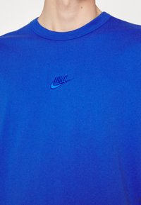 Karališkai mėlynas medvilninis marškinėliai su apvaliu kaklu; krūtinėje yra šiek tiek tamsesniame mėlyne išsiuvinėtas Nike logotipas.