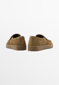 Braune Wildlederschuhe von hinten betrachtet, mit einem schlichten Design und einer dicken Gummisohle, vor einem schlichten weißen Hintergrund.