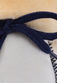 Beiges Wildledermaterial mit Wollfutter und dunkelblauen geflochtenen Schnürsenkeln, das eine strukturierte Oberfläche und ein sicheres Knotendetail zeigt.