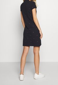 Marinblå polo klänning med korta ärmar, prydd med ett mönster av små röda och vita geometriska figurer. Bärs med vita sneakers.