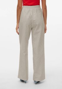 Beige vide bukser med lodrette sorte striber, med høj talje og blød tekstur, parret med lyseblå hæle.