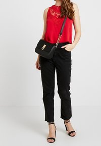 Top rosso senza maniche con dettagli in pizzo, abbinato a jeans neri a vita alta e una borsa a tracolla nera con chiusura dorata. Tacchi neri con cinturini.