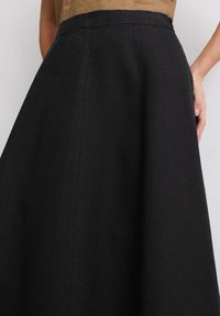 Jupe longue noire en A, fabriquée dans un tissu texturé, dotée d'une taille lisse et de détails de couture verticaux. Convient à diverses occasions.