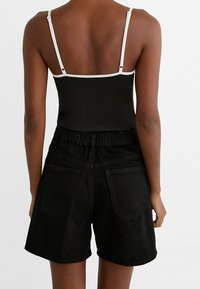 Bodysuit negro con tirantes blancos, combinado con unos shorts de mezclilla negros de talle alto con un ajuste relajado y dos bolsillos traseros.