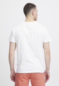 Weißes Baumwoll-T-Shirt mit kurzen Ärmeln und Rundhalsausschnitt. Schlichter Rückansicht, getragen mit hellen Hosen. Dezentes Markenlabel am Saum.