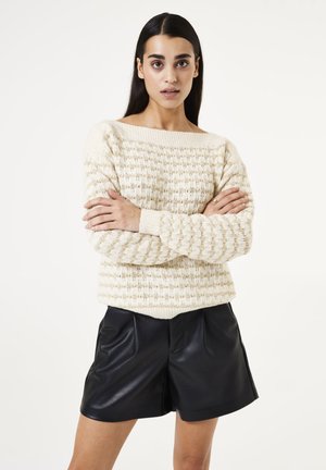 Strickpullover in Creme mit geripptem Halsauschnitt und strukturiertem Muster, kombiniert mit schwarzen Leder-Shorts mit Faltendetails.