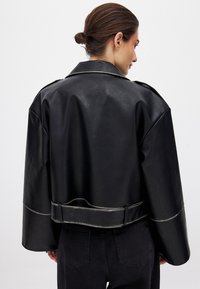 Must hästnahk-jakk musta värviga, laia kraega, lühendatud disainiga ja hõbedaste aktsentidega. Omab vööd ning struktureeritud õlavarre detaile.