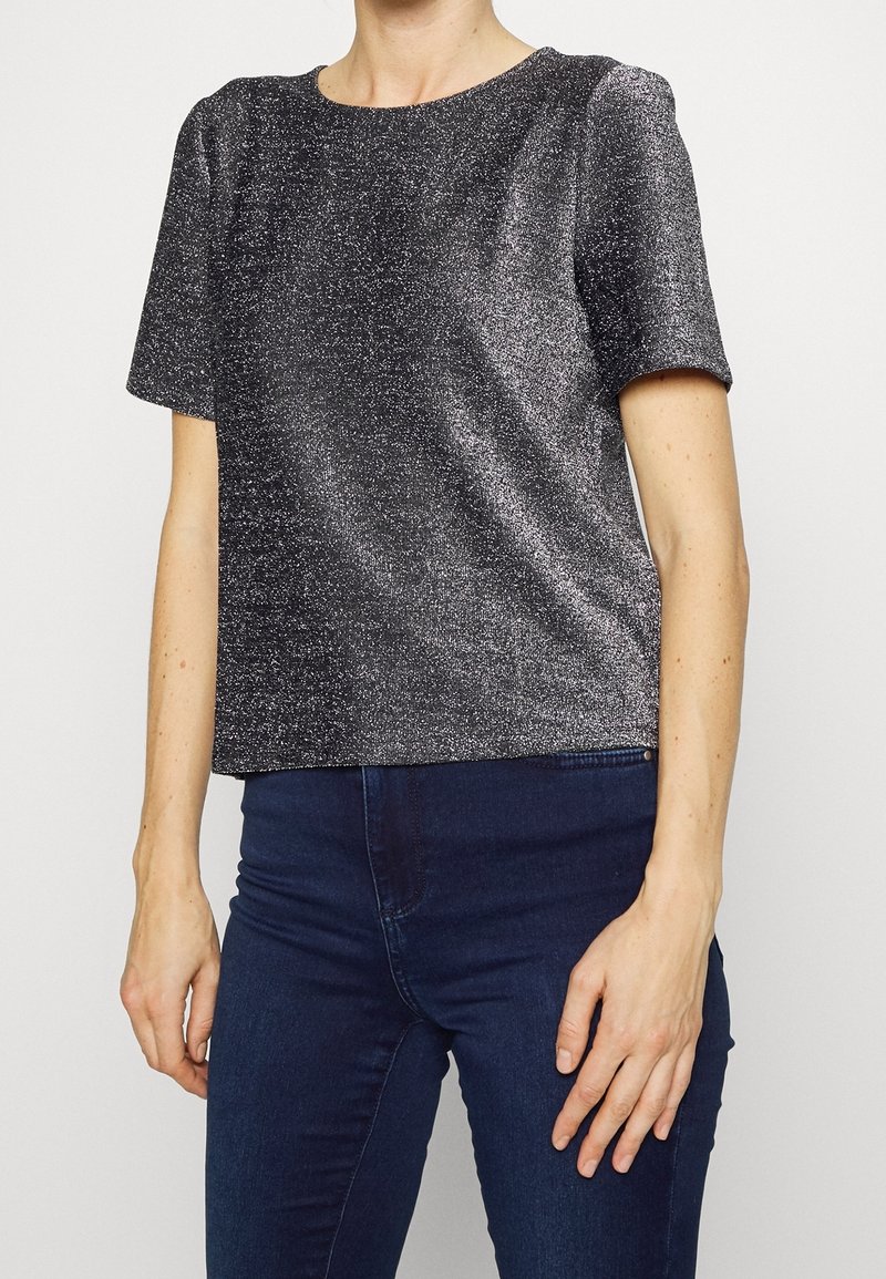 Korte mouwen zwarte top met een glinsterende textuur, ronde halslijn en een relaxte pasvorm, gecombineerd met donkere denim jeans.